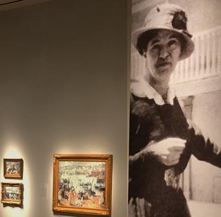 Large exhibition photo of E. Charton Fortune along side of some of her Cornwall paintings