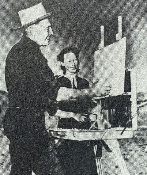 John W. Hilton painting at his easel with his second wife Barbara looking on