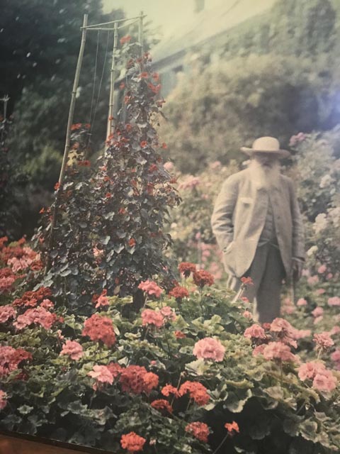 Claude Monet in a white hat with roses by his home at Giverny