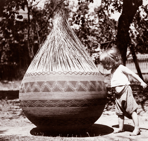 Pomo child next to a large partially woven basket