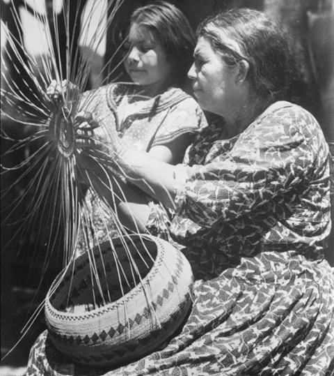 Pomo Indian woman teaching a child the art of basket weaving